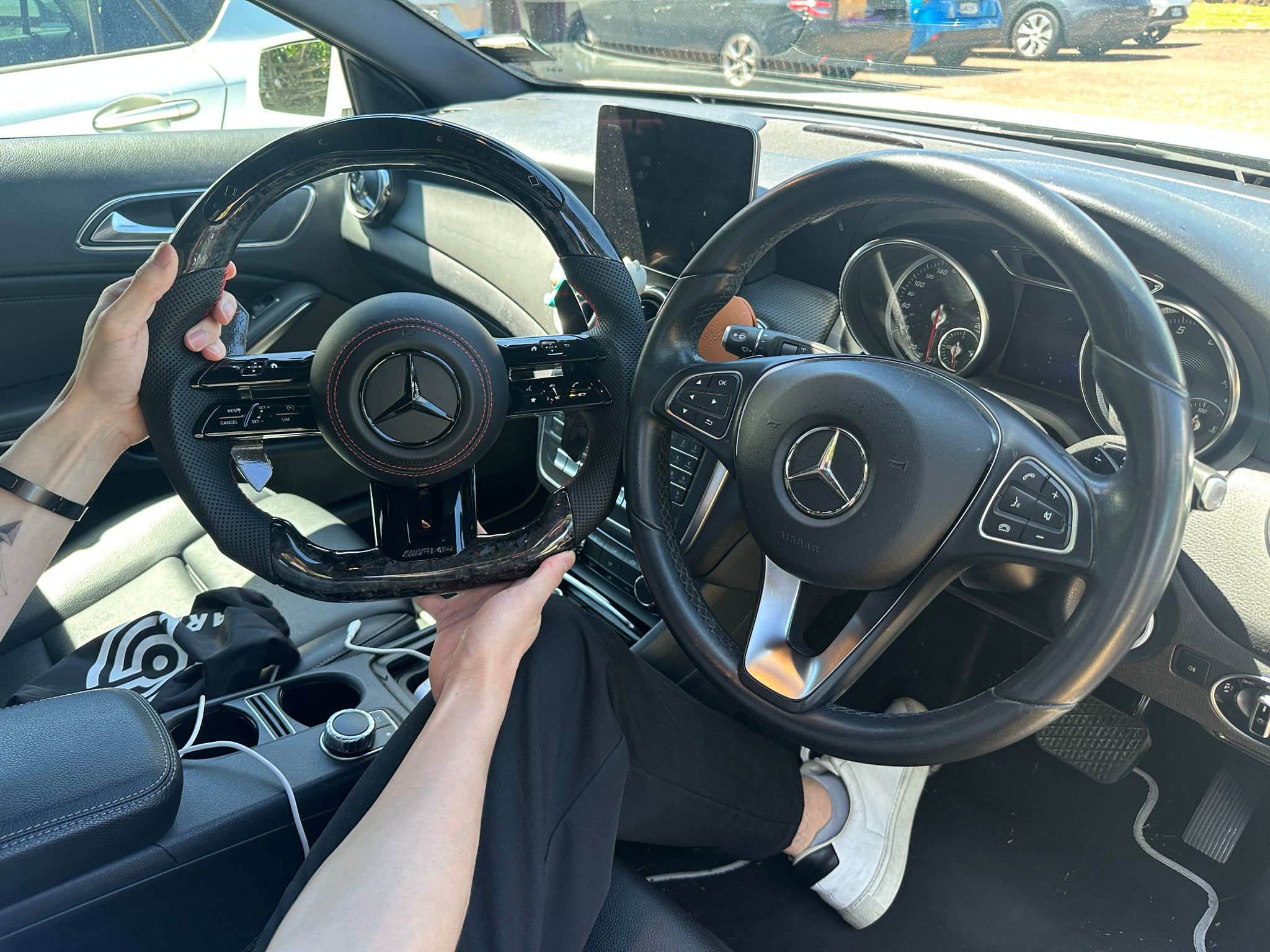 Mercedes interior showing comparison between stock steering wheel and carbon fiber steering wheel