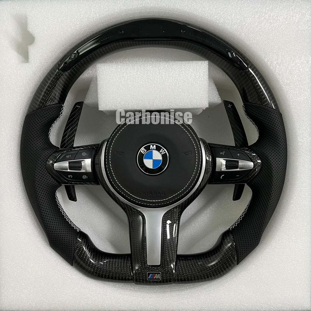Custom BMW M Performance steering wheel featuring a gloss carbon fiber top and bottom, black perforated leather side grips with white contrast stitching, and matching carbon fiber paddle shifters.