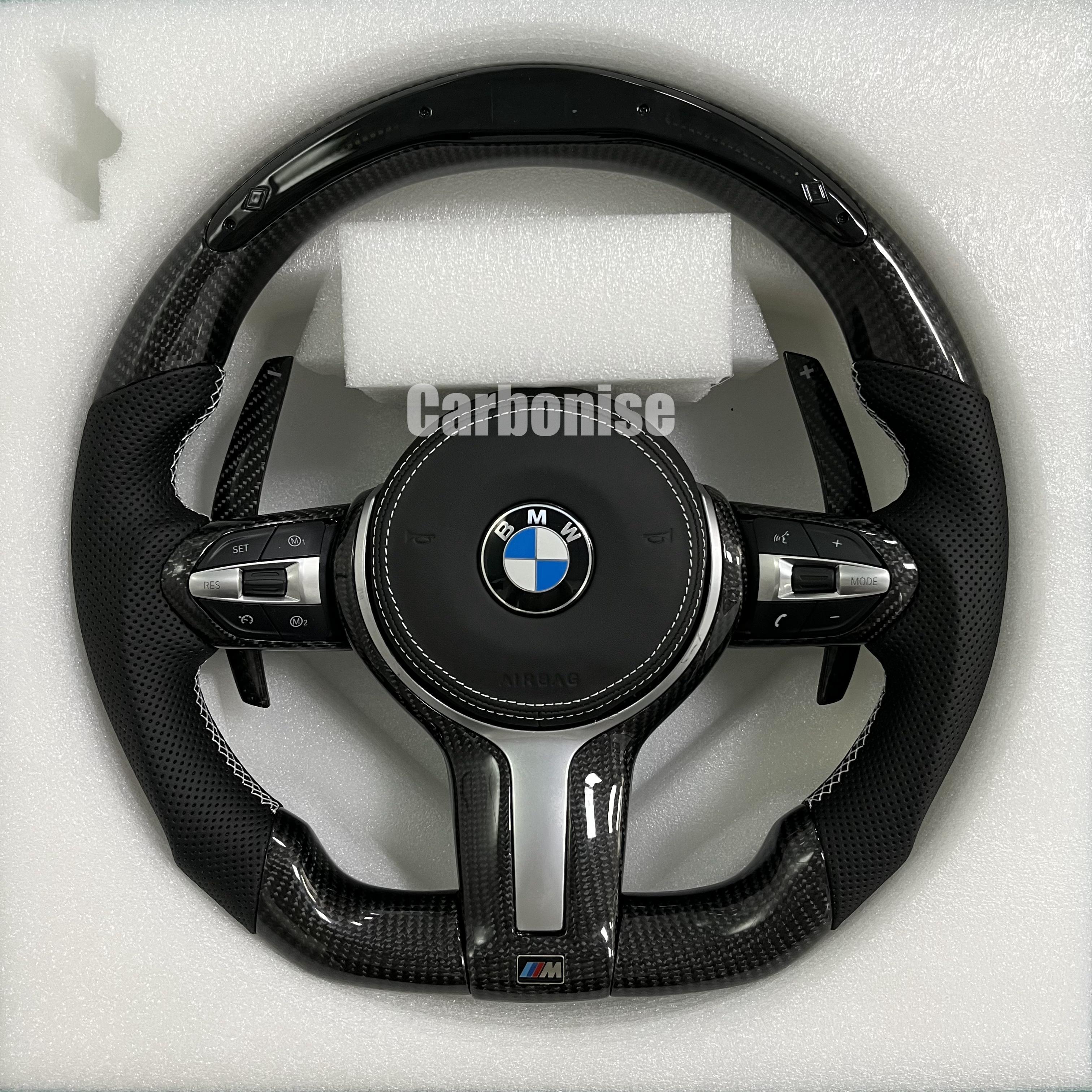 Custom BMW M Performance steering wheel featuring a gloss carbon fiber top and bottom, black perforated leather side grips with white contrast stitching, and matching carbon fiber paddle shifters.