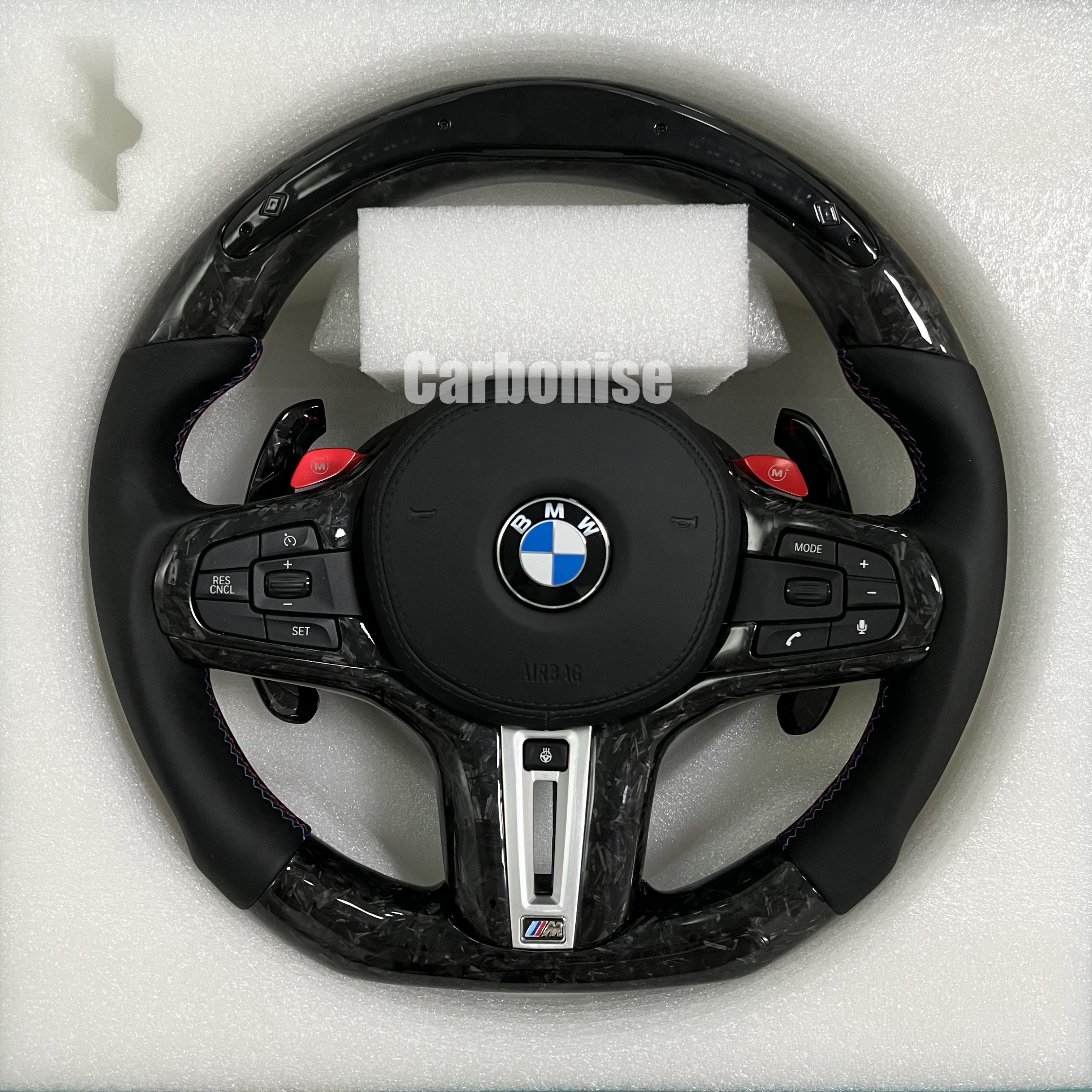 Custom BMW M performance steering wheel featuring a forged carbon fiber finish, black smooth leather side grips, and vibrant red M1 and M2 button accents.