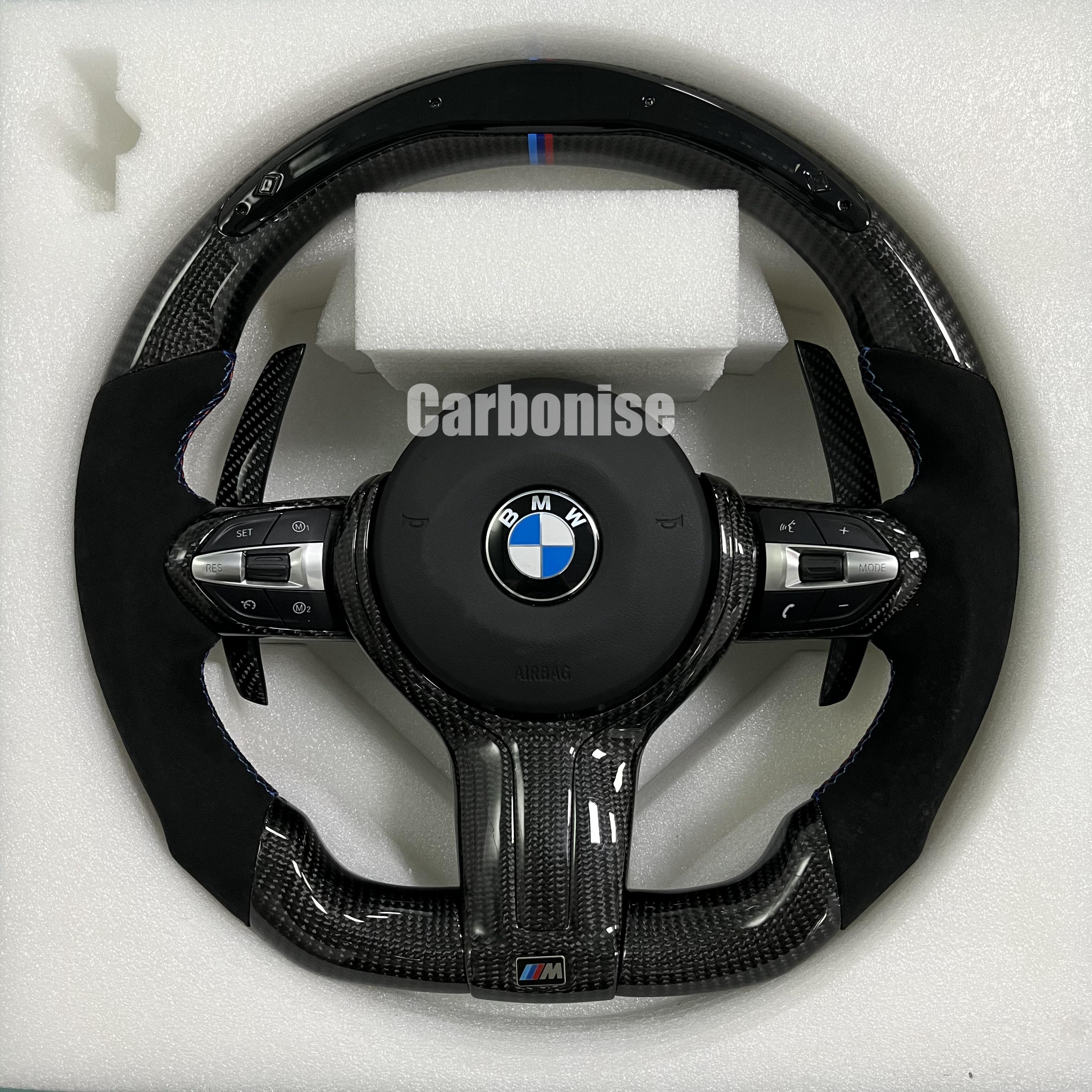 Custom BMW M performance steering wheel featuring high-gloss carbon fiber, black Alcantara grips, blue contrast stitching, and a blue top racing stripe.