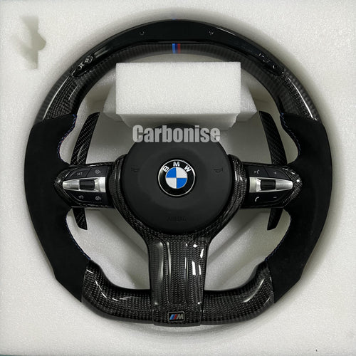 Custom BMW M performance steering wheel featuring high-gloss carbon fiber, black Alcantara grips, blue contrast stitching, and a blue top racing stripe.