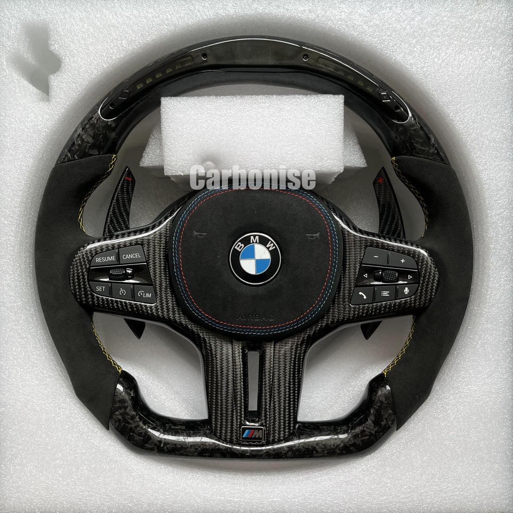 Custom BMW M performance steering wheel featuring a forged carbon fiber finish, a digital LED display, black Alcantara grips, and yellow stitching.