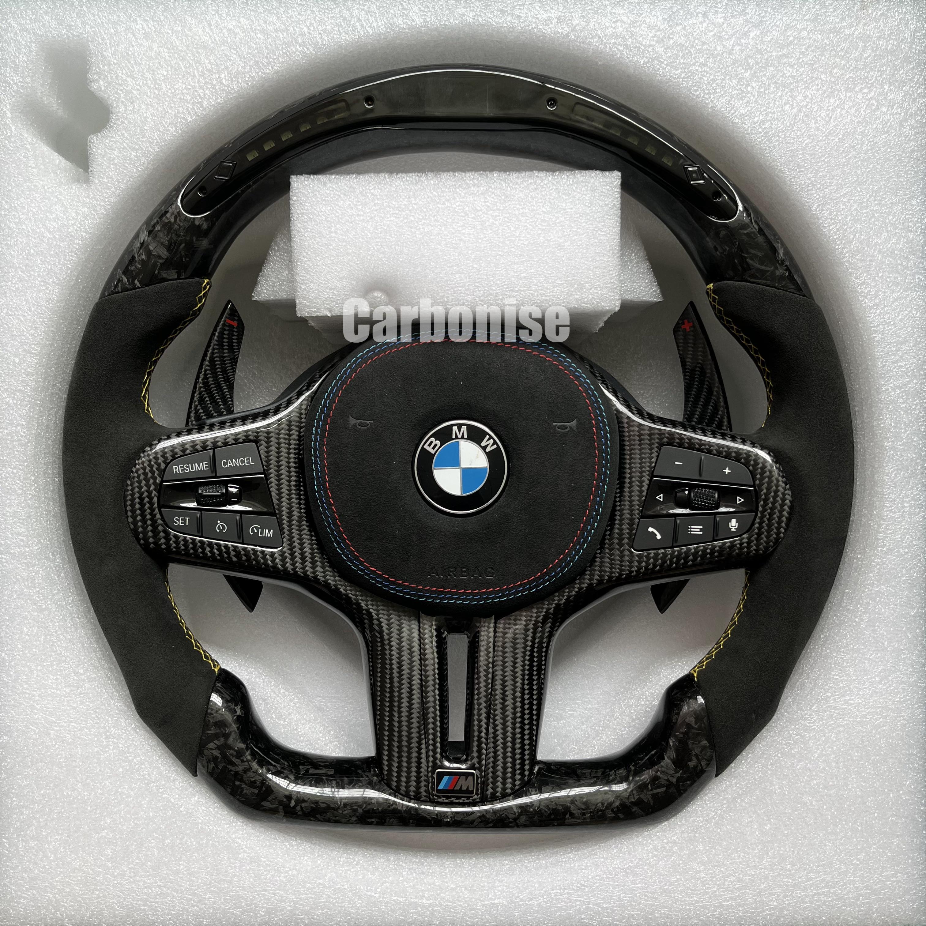 Custom BMW M performance steering wheel featuring a forged carbon fiber finish, a digital LED display, black Alcantara grips, and yellow stitching.