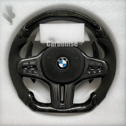 Custom BMW M performance steering wheel featuring a forged carbon fiber finish, a digital LED display, black Alcantara grips, and yellow stitching.