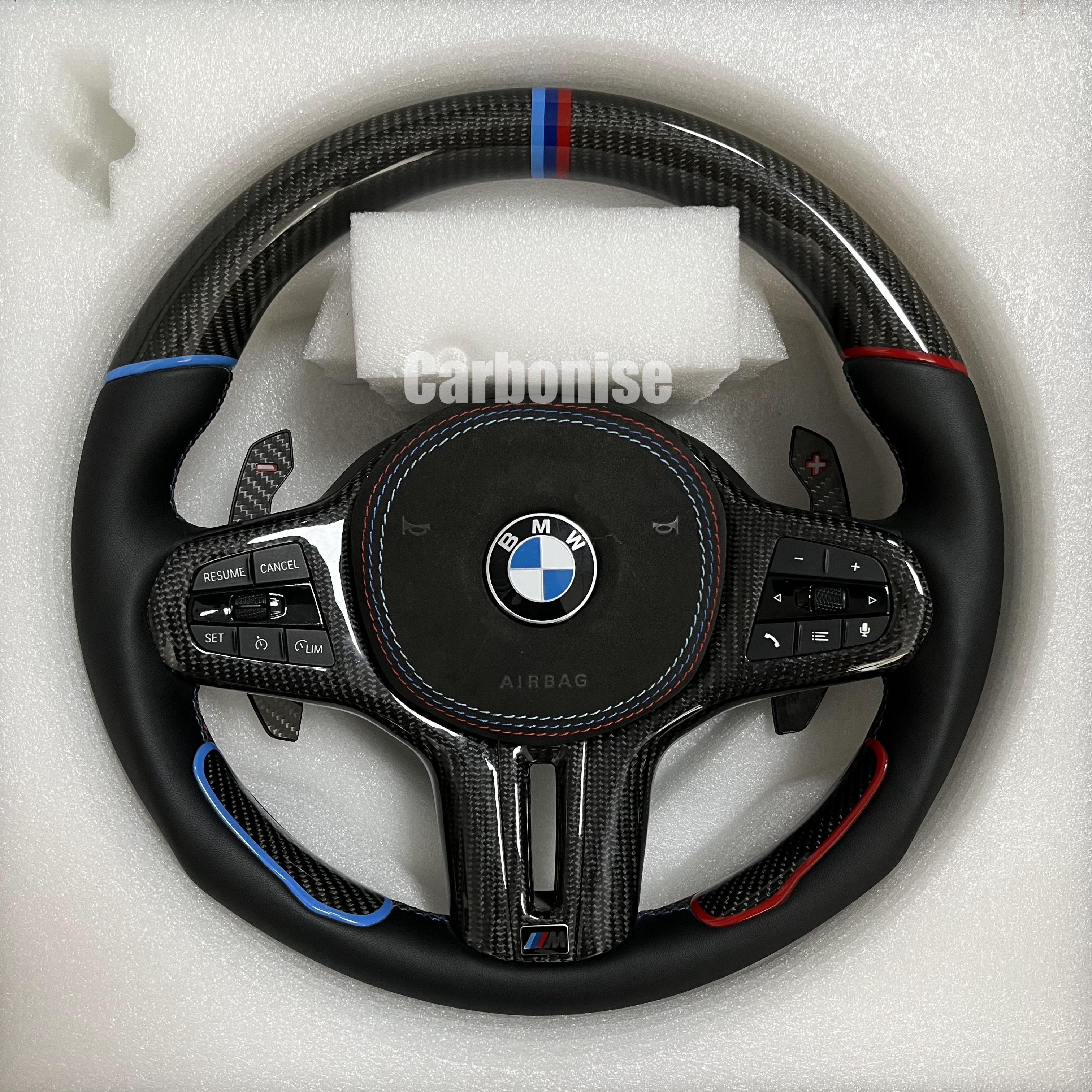Custom BMW M steering wheel featuring gloss carbon fiber, a tri-color top racing stripe, and smooth leather grips with blue and red tinted accents.