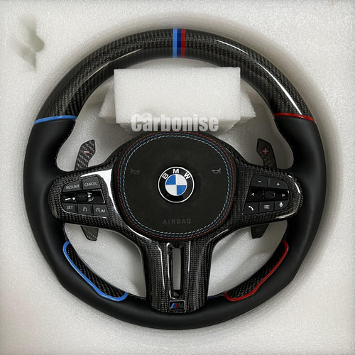 Custom BMW M steering wheel featuring gloss carbon fiber, a tri-color top racing stripe, and smooth leather grips with blue and red tinted accents.