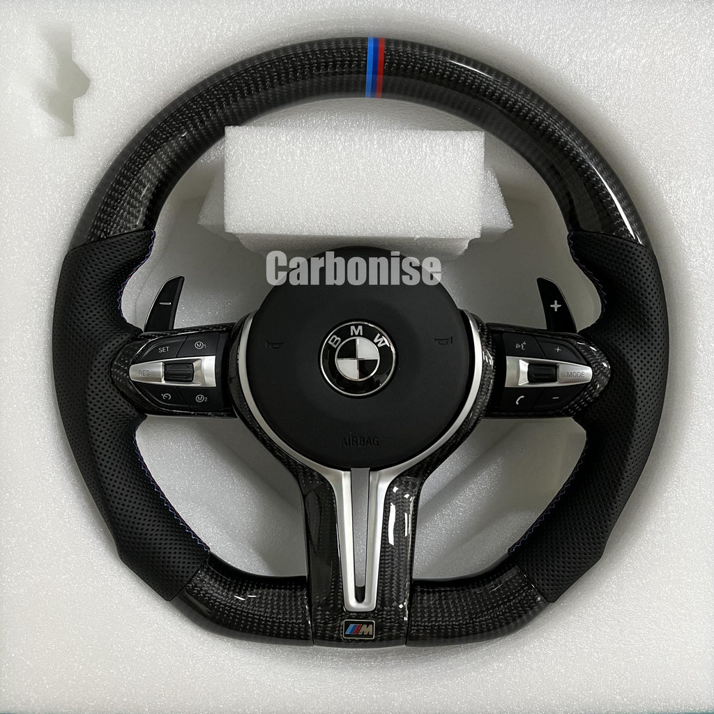 Custom BMW M Performance steering wheel featuring gloss carbon fiber, a signature blue, light blue, and red M-tri color top racing stripe, and black perforated leather side grips with blue contrast stitching.