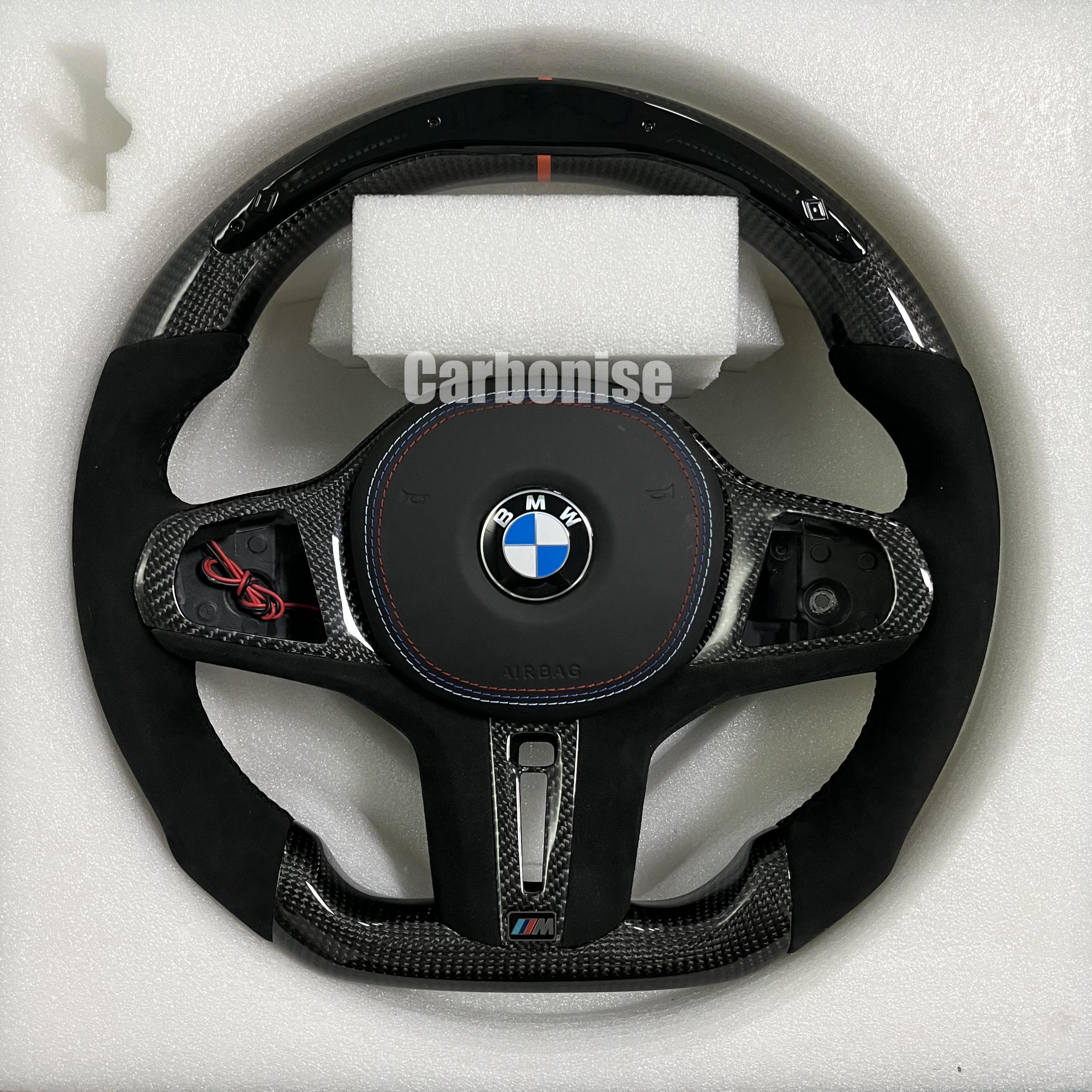 Custom BMW M performance steering wheel featuring high-gloss carbon fiber, black Alcantara side grips, and a vibrant orange top racing stripe.
