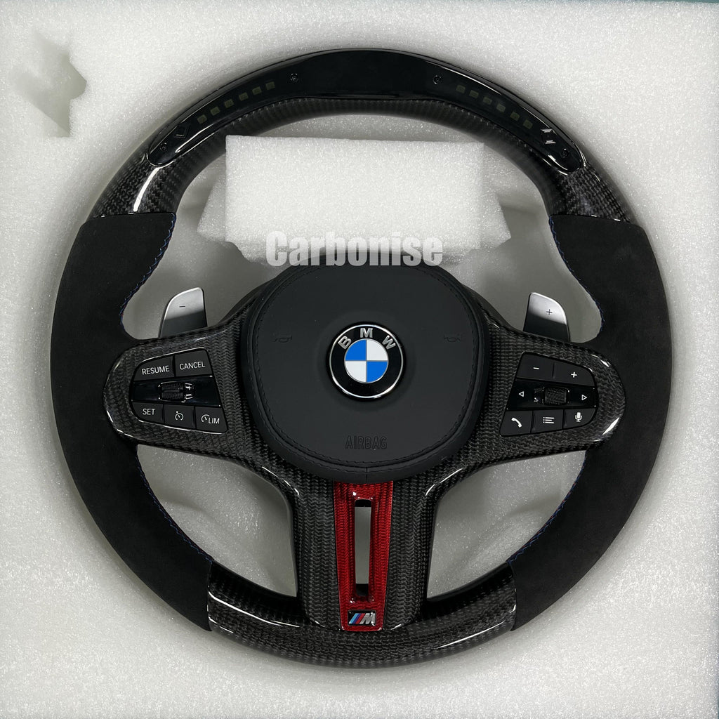 Custom BMW M performance steering wheel featuring gloss carbon fiber with a digital LED shift display, red tinted accents, and black Alcantara side grips.