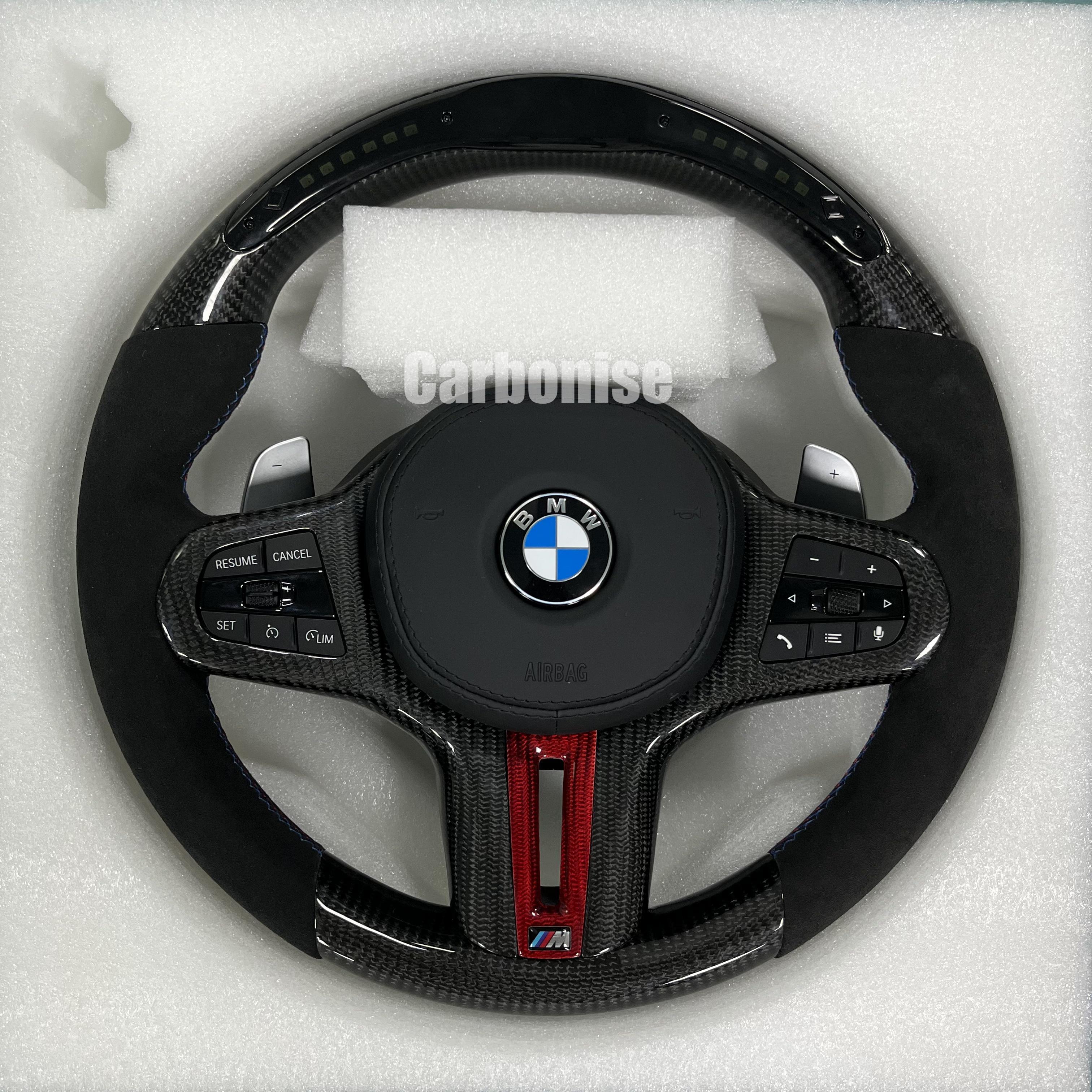 Custom BMW M performance steering wheel featuring gloss carbon fiber with a digital LED shift display, red tinted accents, and black Alcantara side grips.