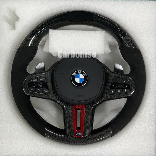 Custom BMW M performance steering wheel featuring gloss carbon fiber with a digital LED shift display, red tinted accents, and black Alcantara side grips.
