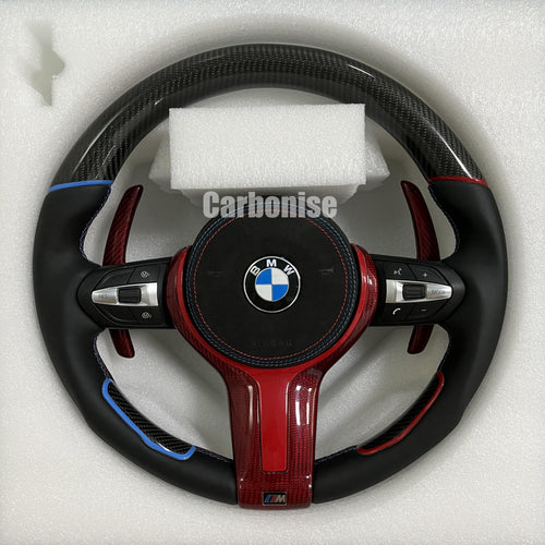 Custom BMW M Performance steering wheel featuring gloss carbon fiber, a split blue and red top racing stripe, black smooth leather grips, and high-gloss red carbon fiber lower trim and paddle shifters.