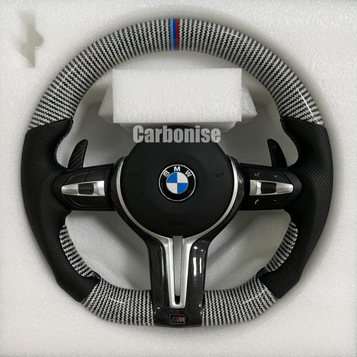 Custom BMW M Performance steering wheel featuring silver twill carbon fiber, a signature M-tri color top racing stripe, and black perforated leather side grips with blue contrast stitching.