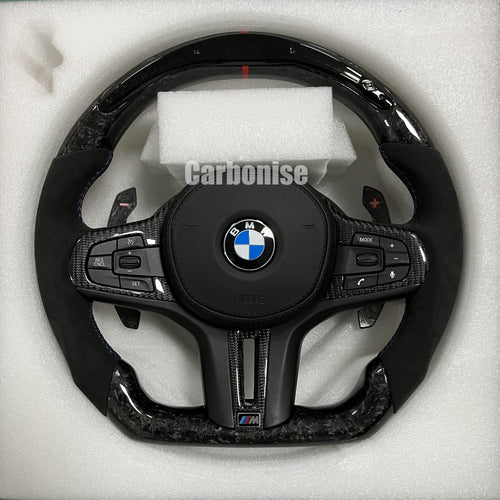 Custom BMW M performance steering wheel featuring a forged carbon fiber finish, black Alcantara side grips, and a vibrant red top racing stripe.