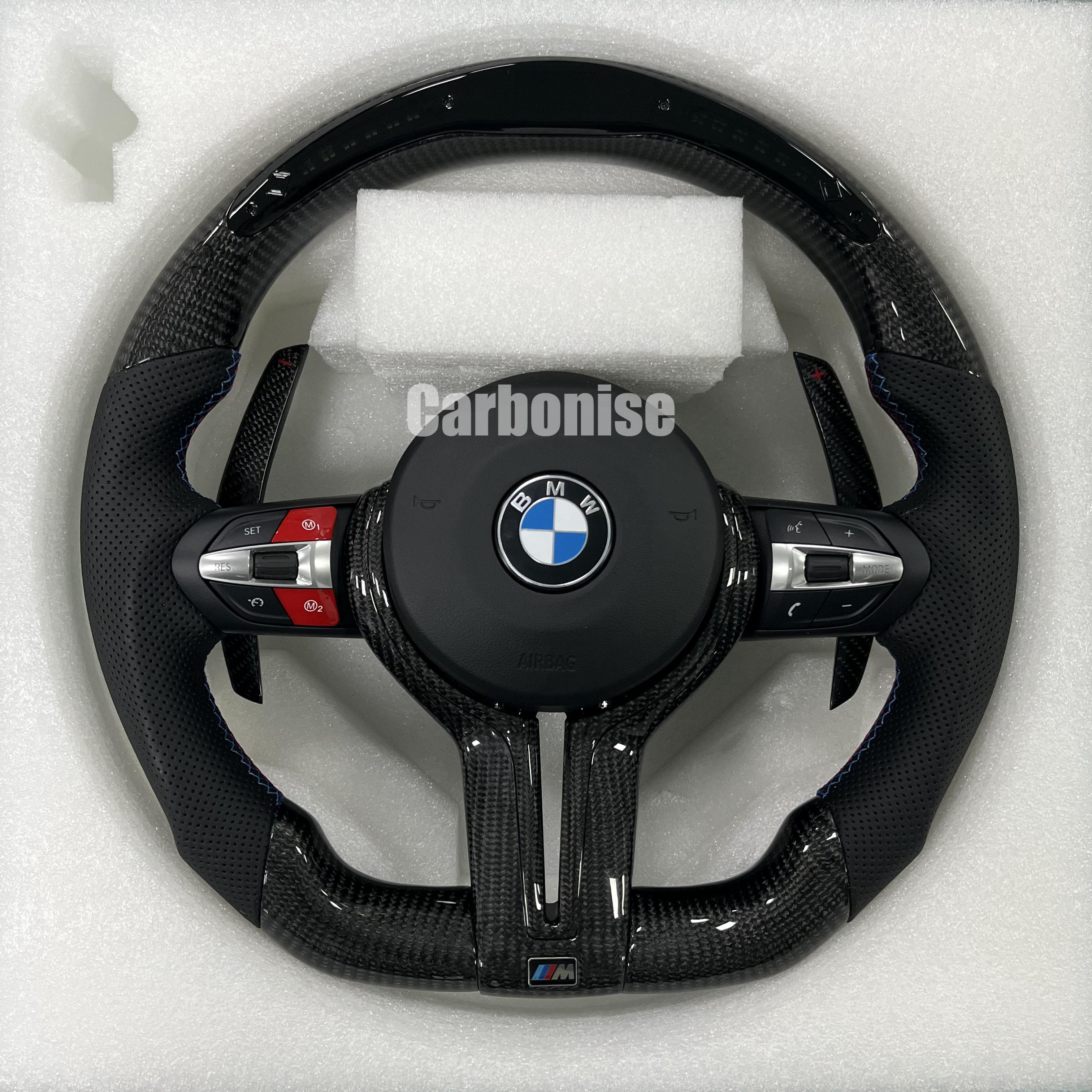 Custom BMW M performance steering wheel featuring gloss carbon fiber, black perforated leather side grips with blue stitching, and red button accents.