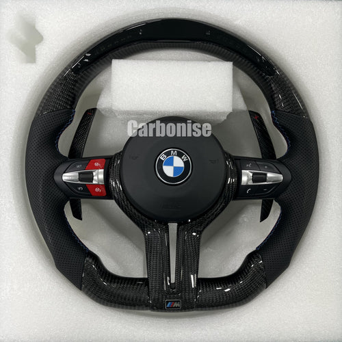 Custom BMW M performance steering wheel featuring gloss carbon fiber, black perforated leather side grips with blue stitching, and red button accents.