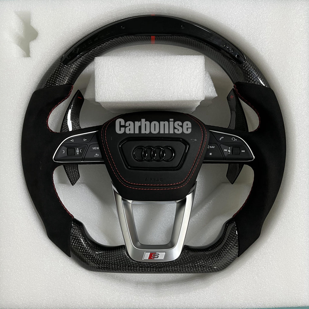 Custom Audi S performance steering wheel with gloss carbon fiber, a red top racing stripe, and black Alcantara side grips with red contrast stitching.