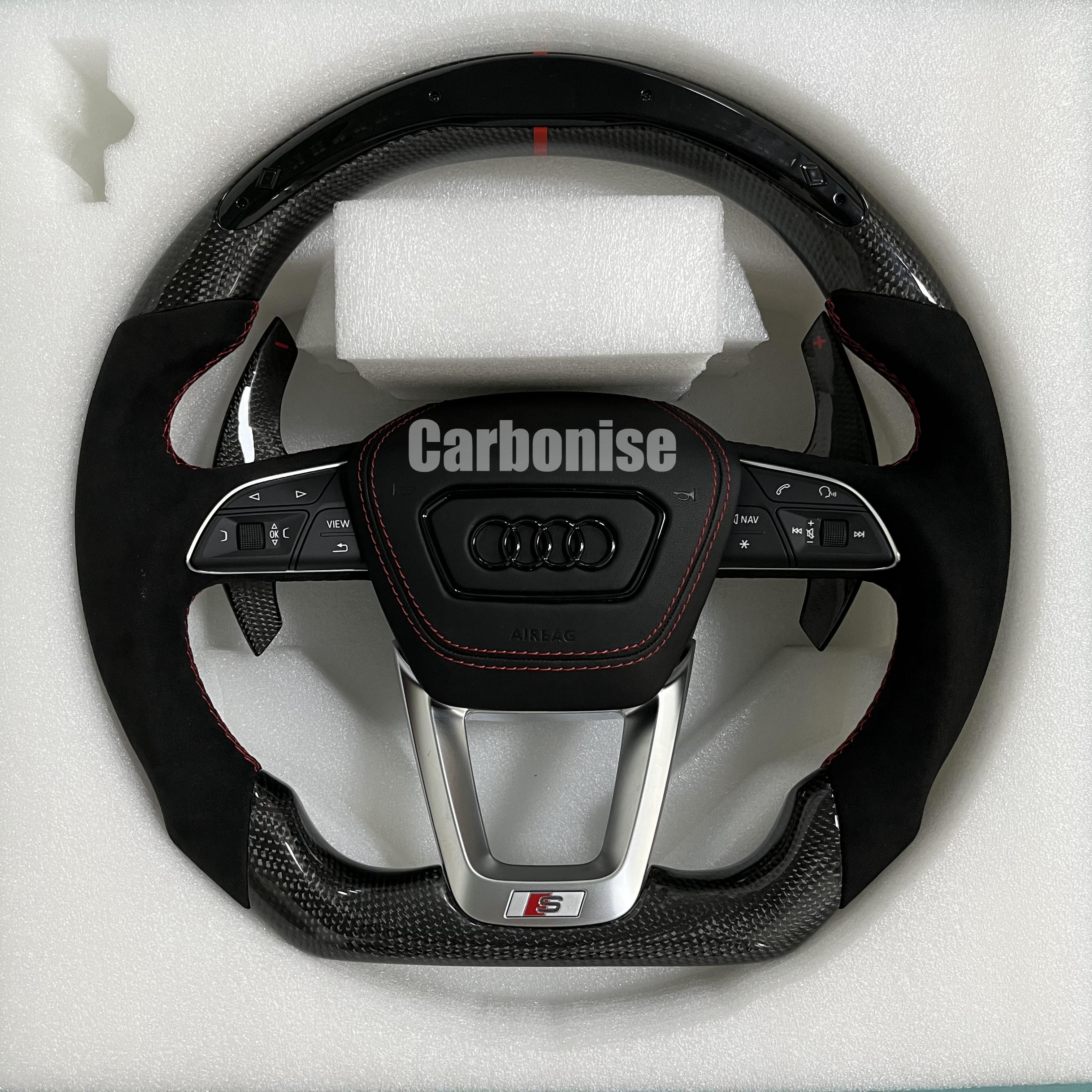 Custom Audi S performance steering wheel with gloss carbon fiber, a red top racing stripe, and black Alcantara side grips with red contrast stitching.