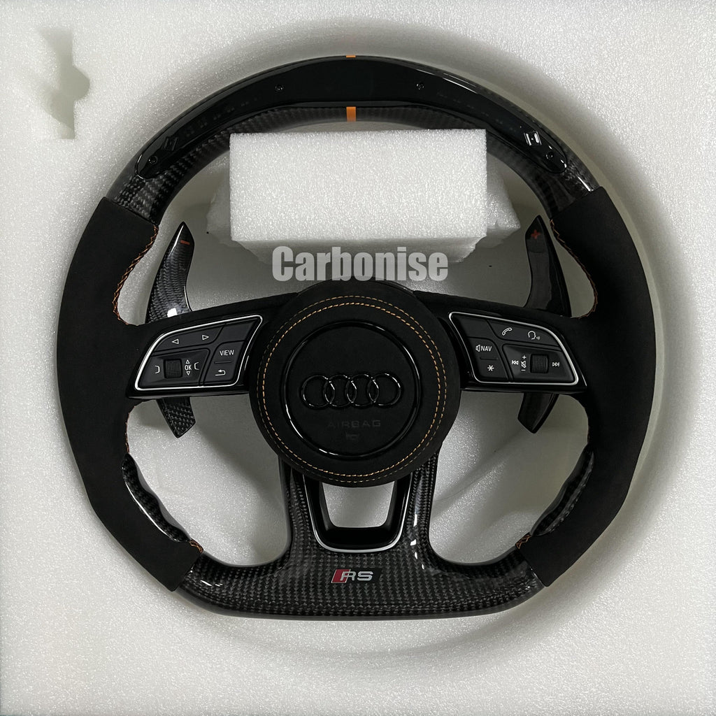 Custom Audi RS steering wheel with high-gloss carbon fiber, an orange top racing stripe, and black Alcantara side grips with orange stitching.