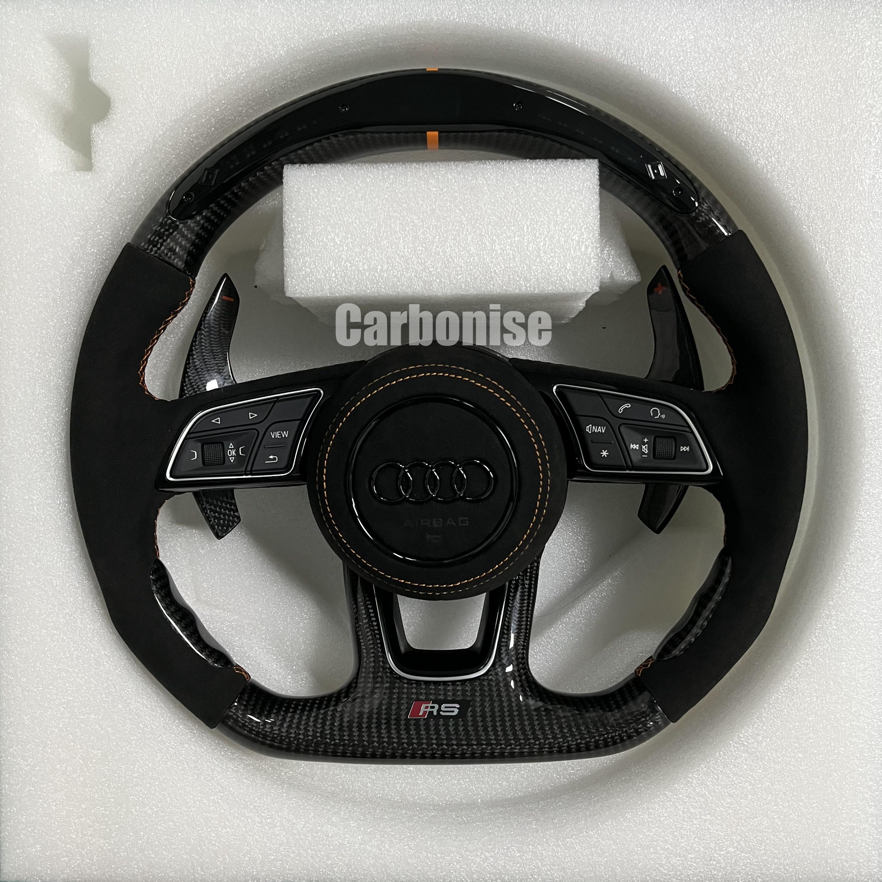 Custom Audi RS steering wheel with high-gloss carbon fiber, an orange top racing stripe, and black Alcantara side grips with orange stitching.