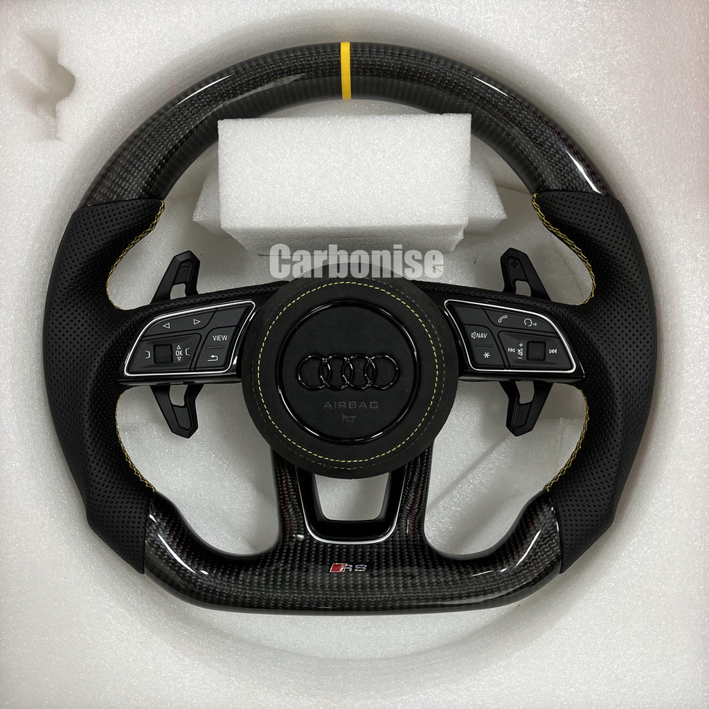 Custom Audi RS carbon fiber steering wheel featuring a yellow top stripe, yellow contrast stitching on perforated leather grips, and a blacked-out center emblem.