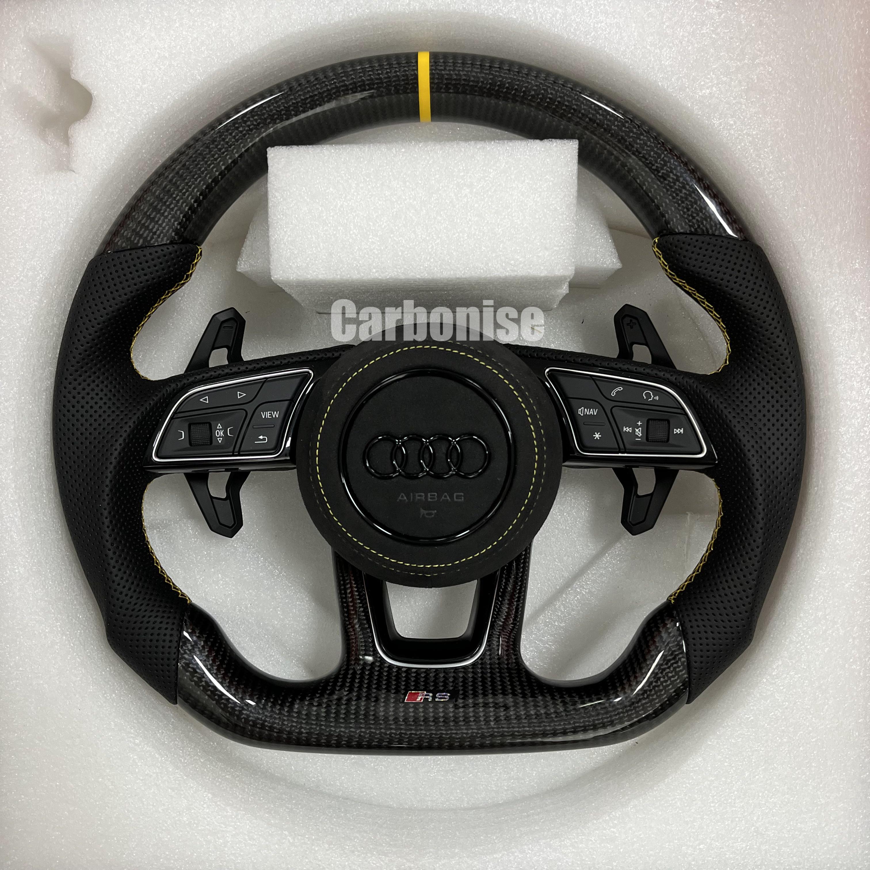 Custom Audi RS carbon fiber steering wheel featuring a yellow top stripe, yellow contrast stitching on perforated leather grips, and a blacked-out center emblem.