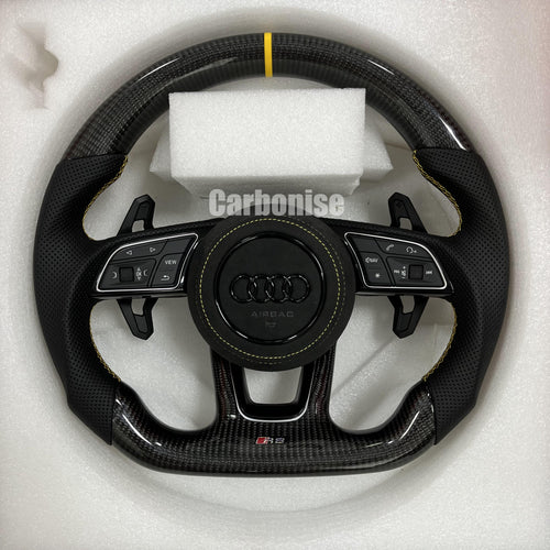 Custom Audi RS carbon fiber steering wheel featuring a yellow top stripe, yellow contrast stitching on perforated leather grips, and a blacked-out center emblem.