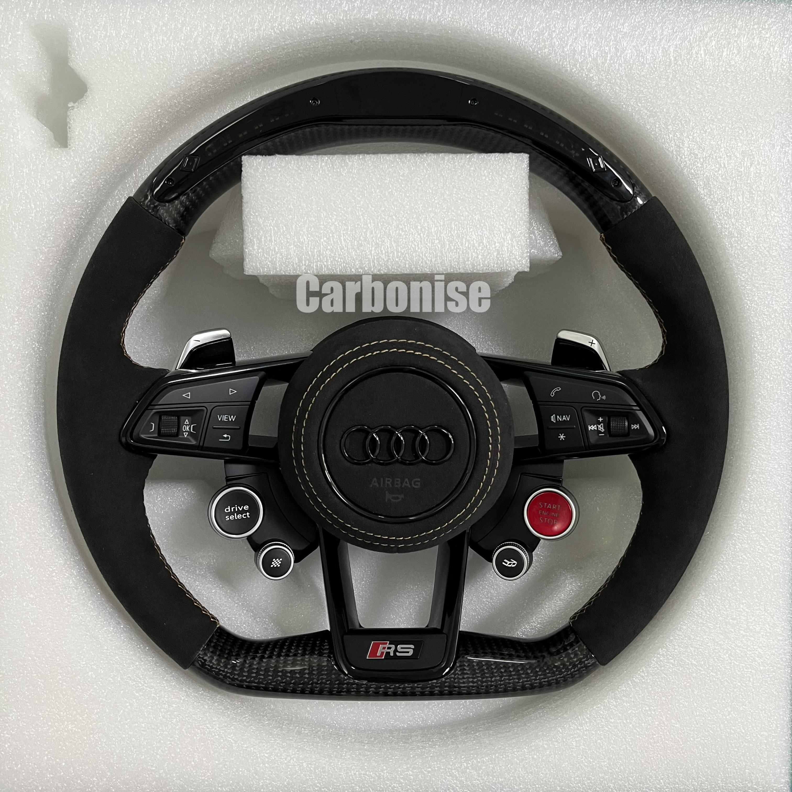 Custom Audi RS carbon fiber steering wheel featuring black Alcantara side grips, gold contrast stitching, and integrated red Start/Stop and black Drive Select buttons.