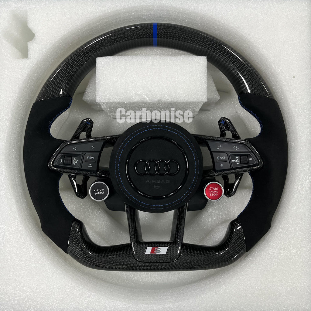 Custom Audi S performance steering wheel featuring gloss carbon fiber, a blue top racing stripe, black Alcantara side grips with blue stitching, and integrated red Start/Stop and black Drive Select buttons.
