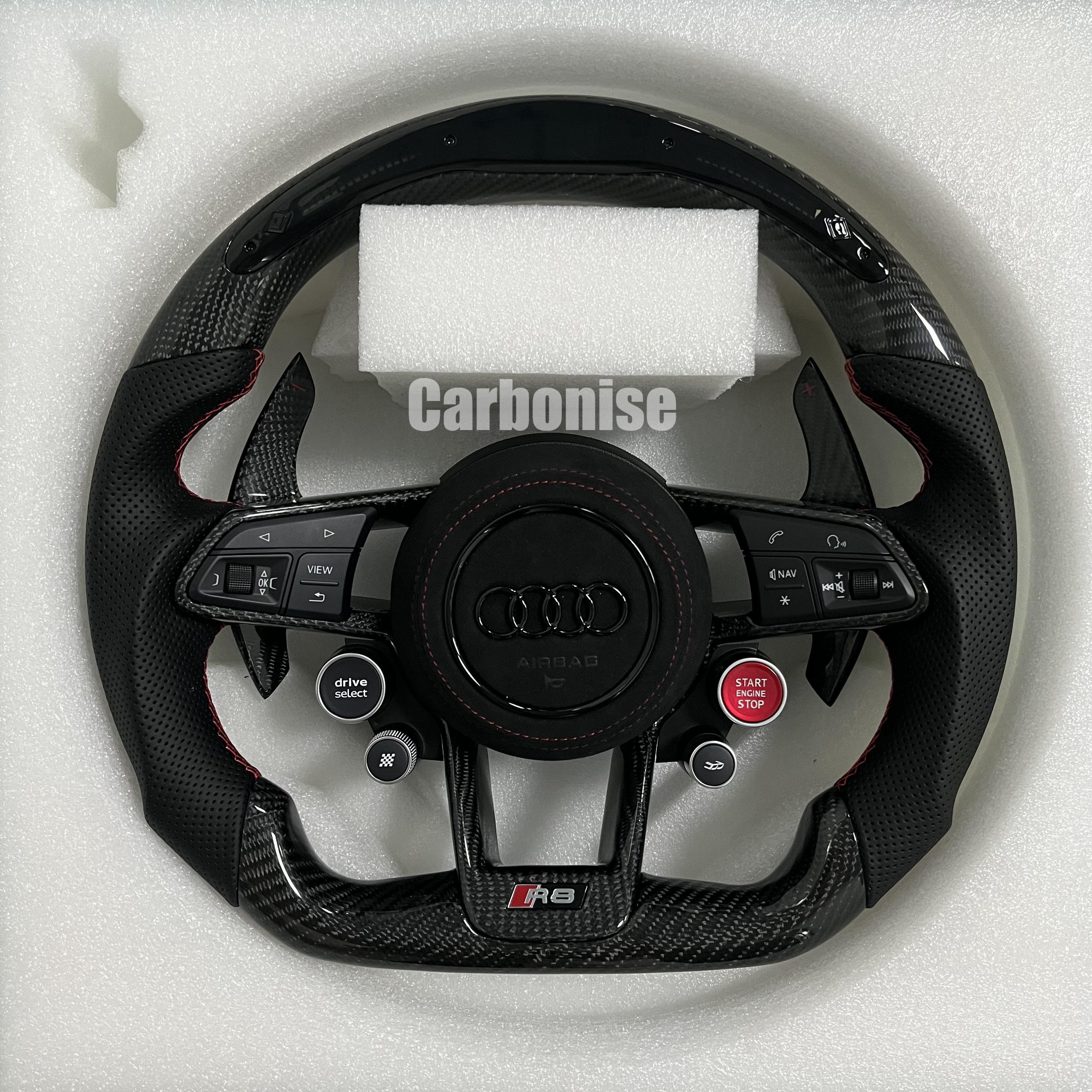 Custom Audi R8 carbon fiber steering wheel featuring integrated red Start/Stop and black Drive Select buttons, perforated leather side grips with red stitching, and a blacked-out center Audi rings emblem.