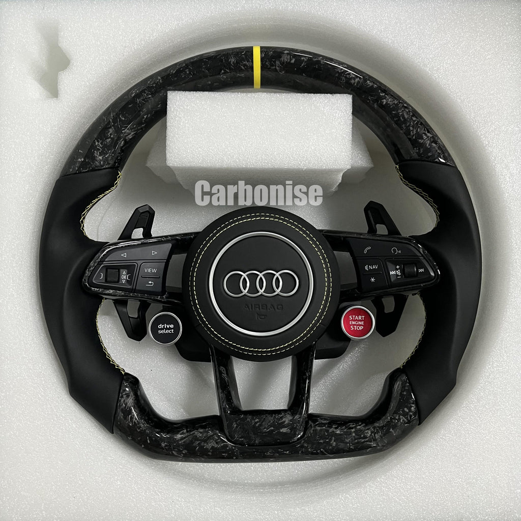 Custom Audi RS steering wheel in forged carbon fiber with a yellow top racing stripe, black smooth leather grips with yellow stitching, and integrated red Start/Stop and black Drive Select buttons.