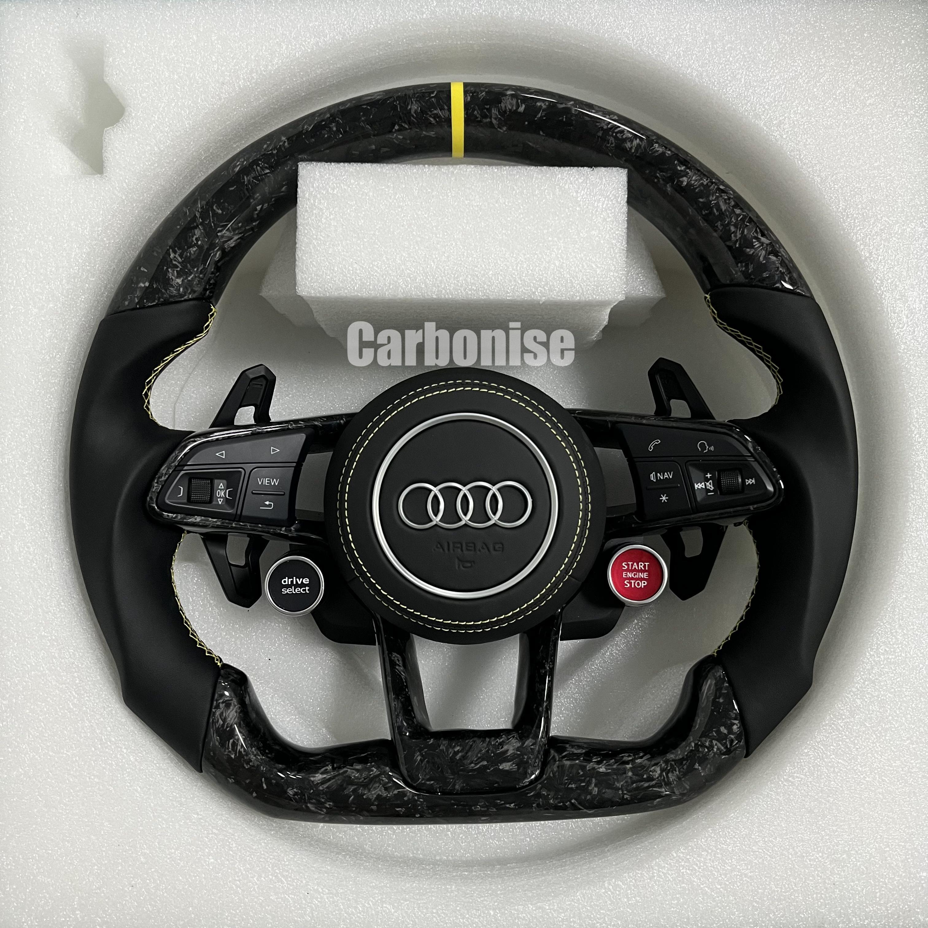 Custom Audi RS steering wheel in forged carbon fiber with a yellow top racing stripe, black smooth leather grips with yellow stitching, and integrated red Start/Stop and black Drive Select buttons.