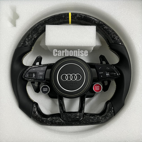 Custom Audi RS steering wheel in forged carbon fiber with a yellow top racing stripe, black smooth leather grips with yellow stitching, and integrated red Start/Stop and black Drive Select buttons.