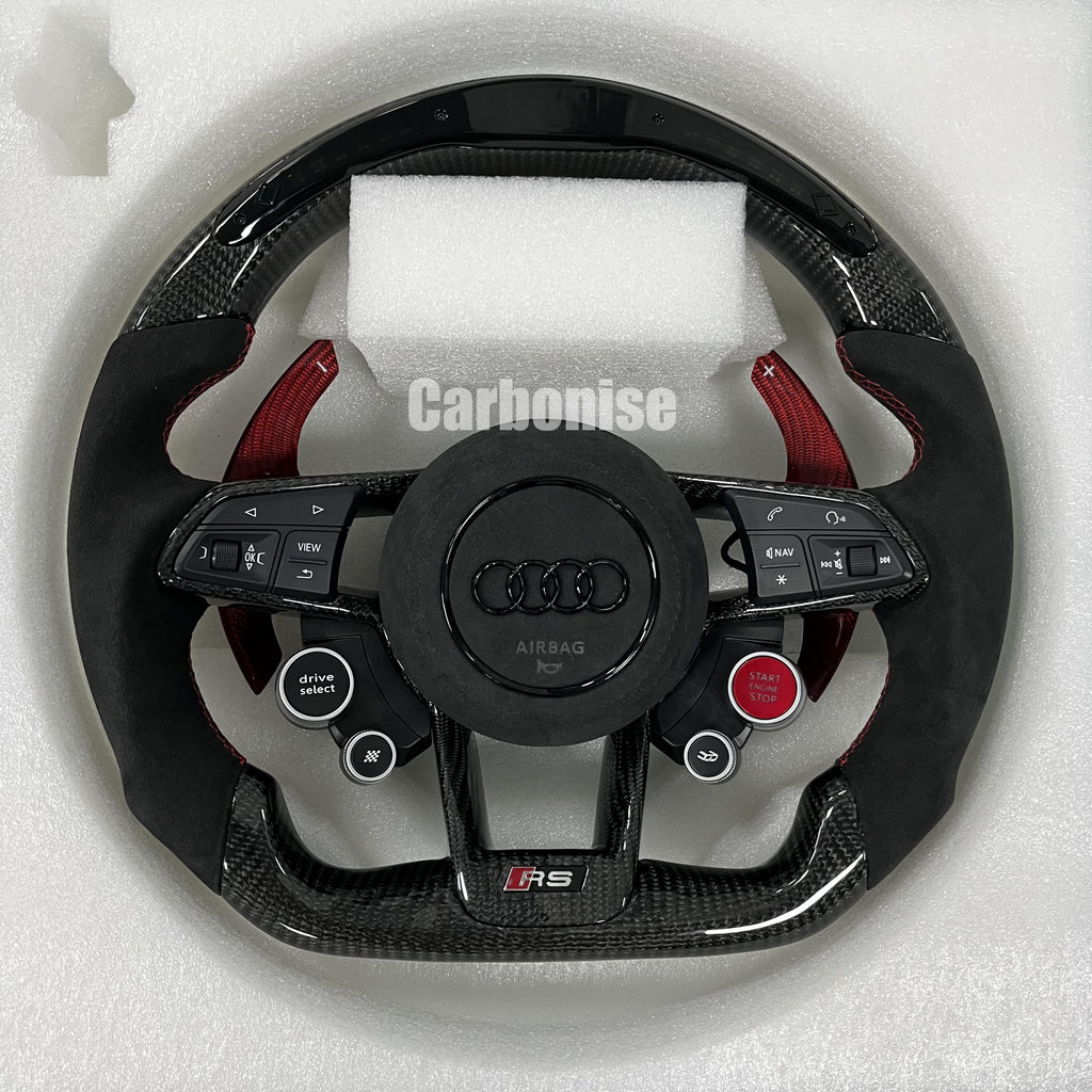 Custom Audi RS steering wheel featuring gloss carbon fiber, red-tinted carbon fiber paddle shifters, black Alcantara grips with red stitching, and integrated performance drive buttons.