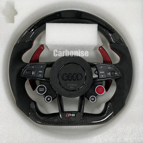 Custom Audi RS steering wheel featuring gloss carbon fiber, red-tinted carbon fiber paddle shifters, black Alcantara grips with red stitching, and integrated performance drive buttons.