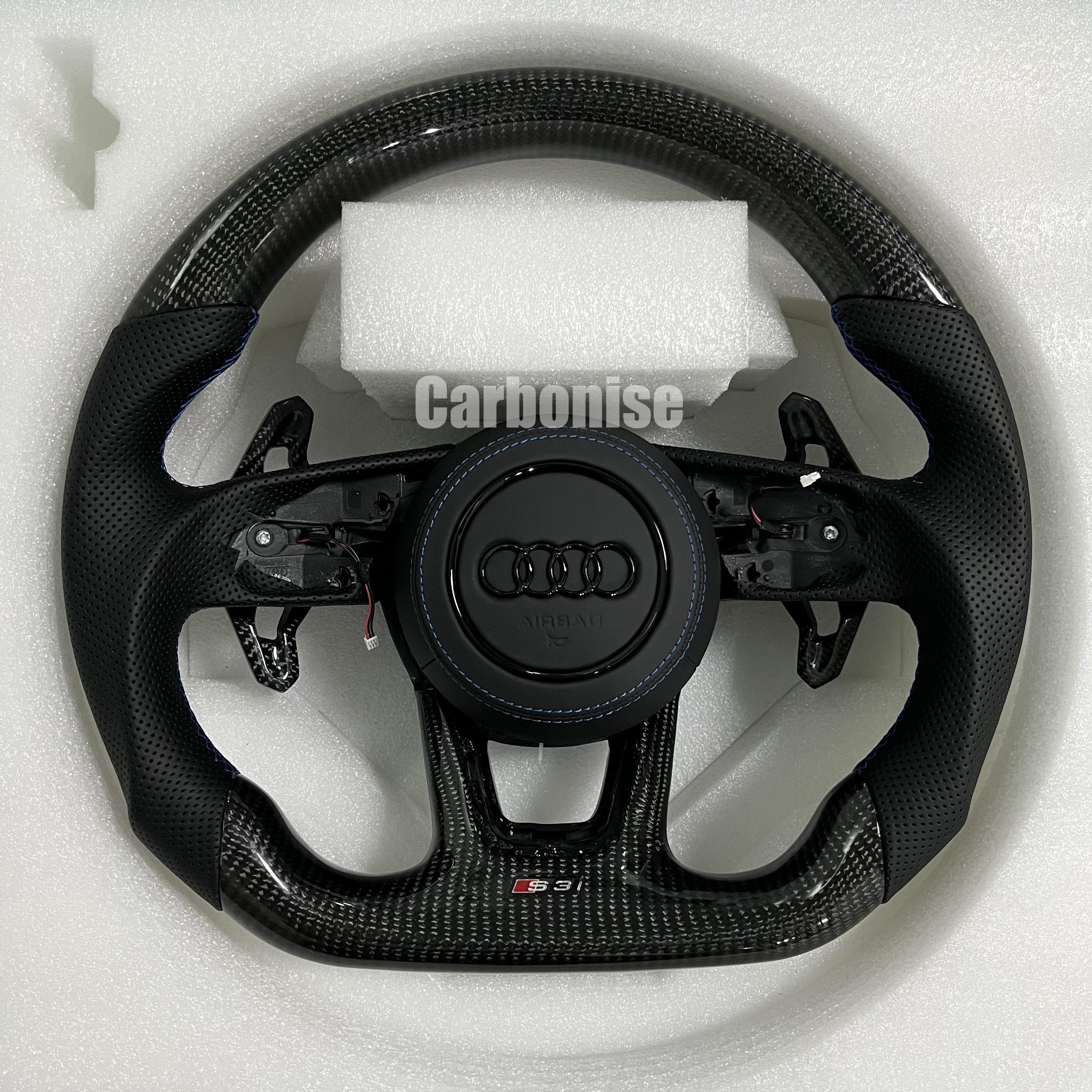 Custom Audi S3 steering wheel featuring gloss carbon fiber, perforated leather side grips with blue stitching, and blacked-out Audi rings on a leather airbag cover.