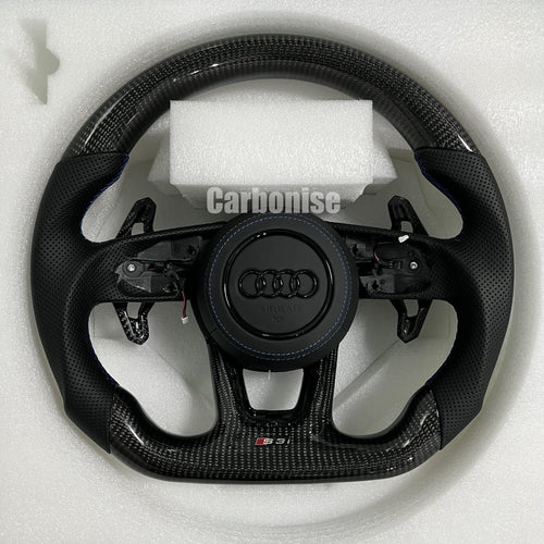 Custom Audi S3 steering wheel featuring gloss carbon fiber, perforated leather side grips with blue stitching, and blacked-out Audi rings on a leather airbag cover.