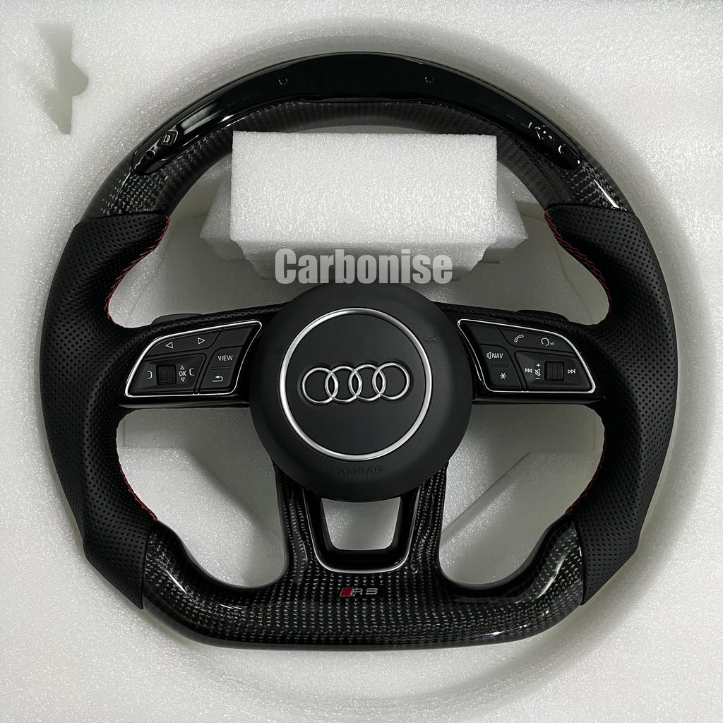 Custom Audi RS steering wheel featuring high-gloss carbon fiber, black perforated leather grips with red stitching, and a center Audi rings emblem.