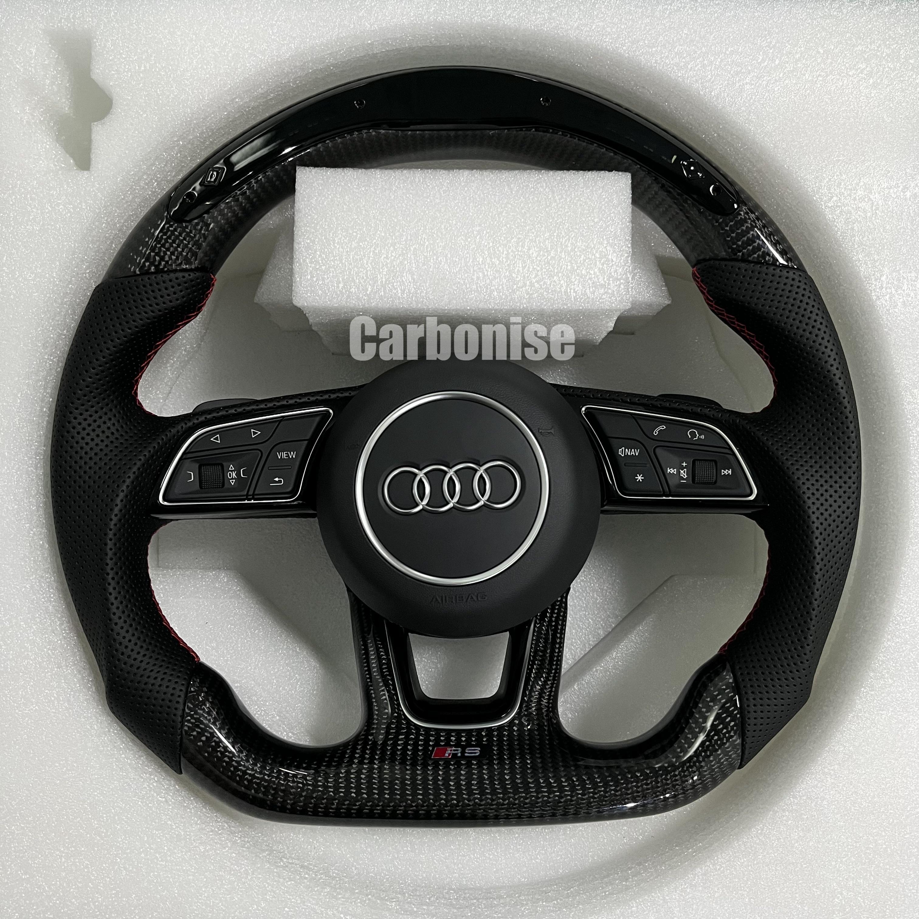Custom Audi RS steering wheel featuring high-gloss carbon fiber, black perforated leather grips with red stitching, and a center Audi rings emblem.