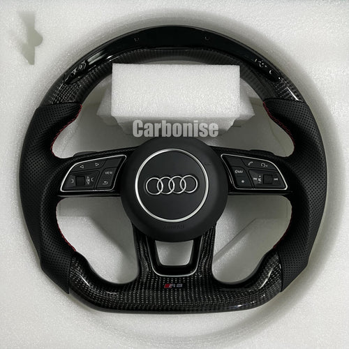 Custom Audi RS steering wheel featuring high-gloss carbon fiber, black perforated leather grips with red stitching, and a center Audi rings emblem.