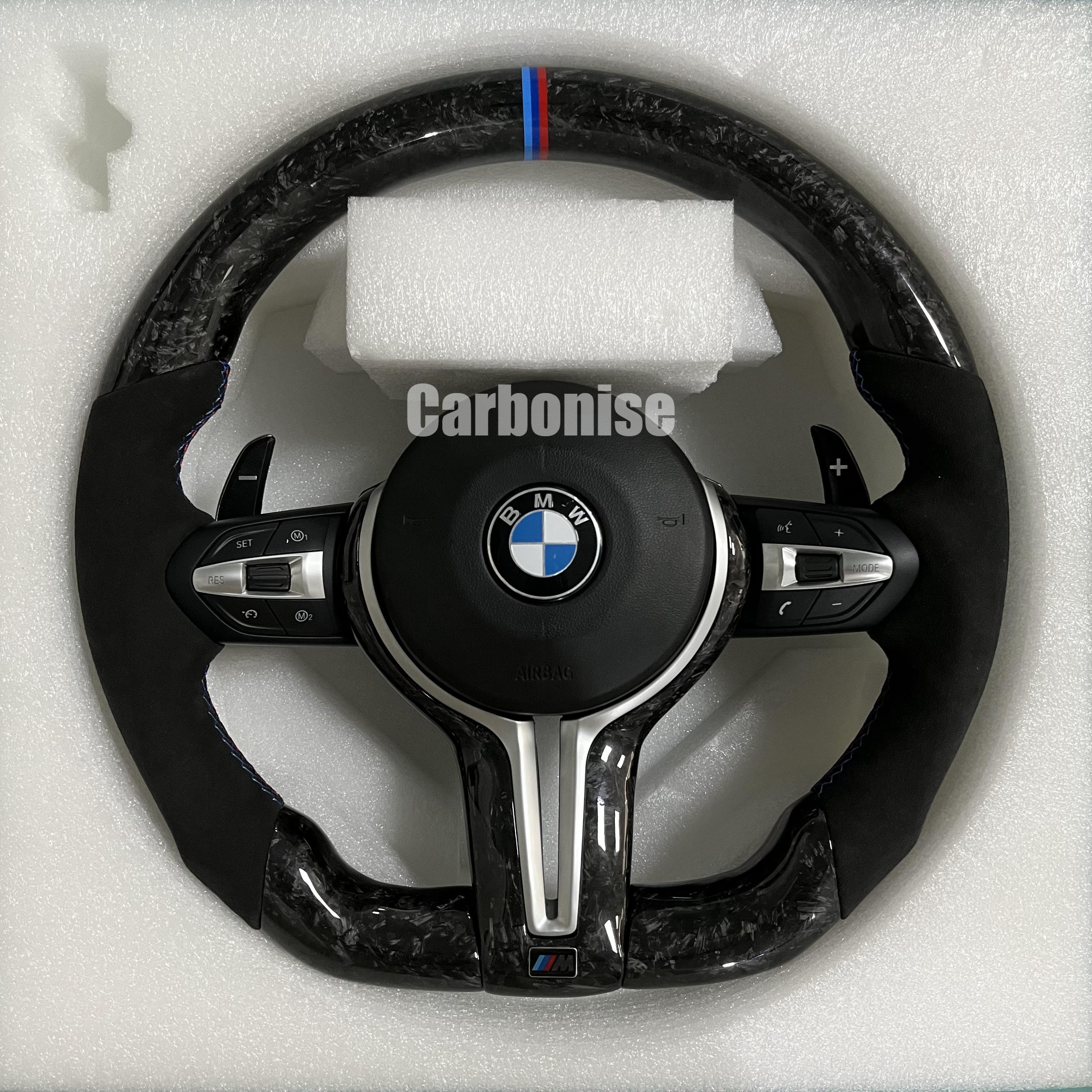 Custom BMW M performance steering wheel featuring a forged carbon fiber finish, black Alcantara side grips, and a signature M-tri color top racing stripe.