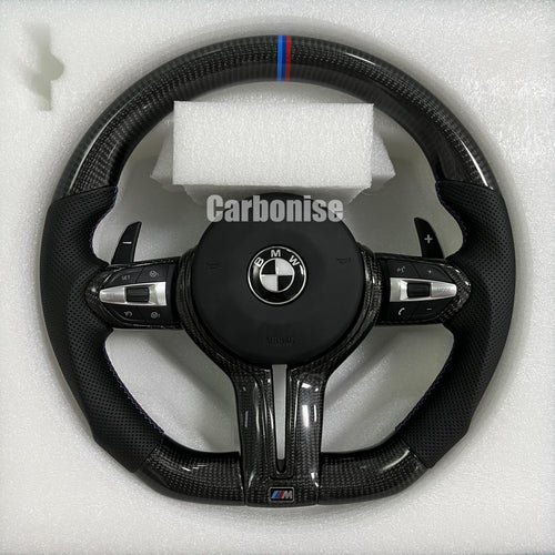 Custom BMW M Performance steering wheel featuring high-gloss twill carbon fiber, a signature blue, light blue, and red M-tri color top racing stripe, and black perforated leather side grips with blue contrast stitching.