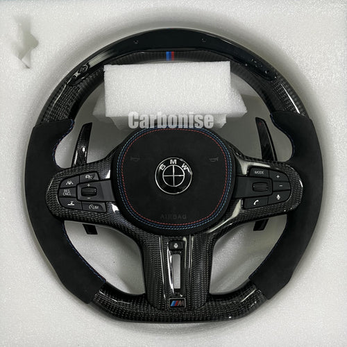 Custom BMW M performance steering wheel featuring high-gloss carbon fiber, black Alcantara side grips with blue stitching, and a signature M-tri color top racing stripe.