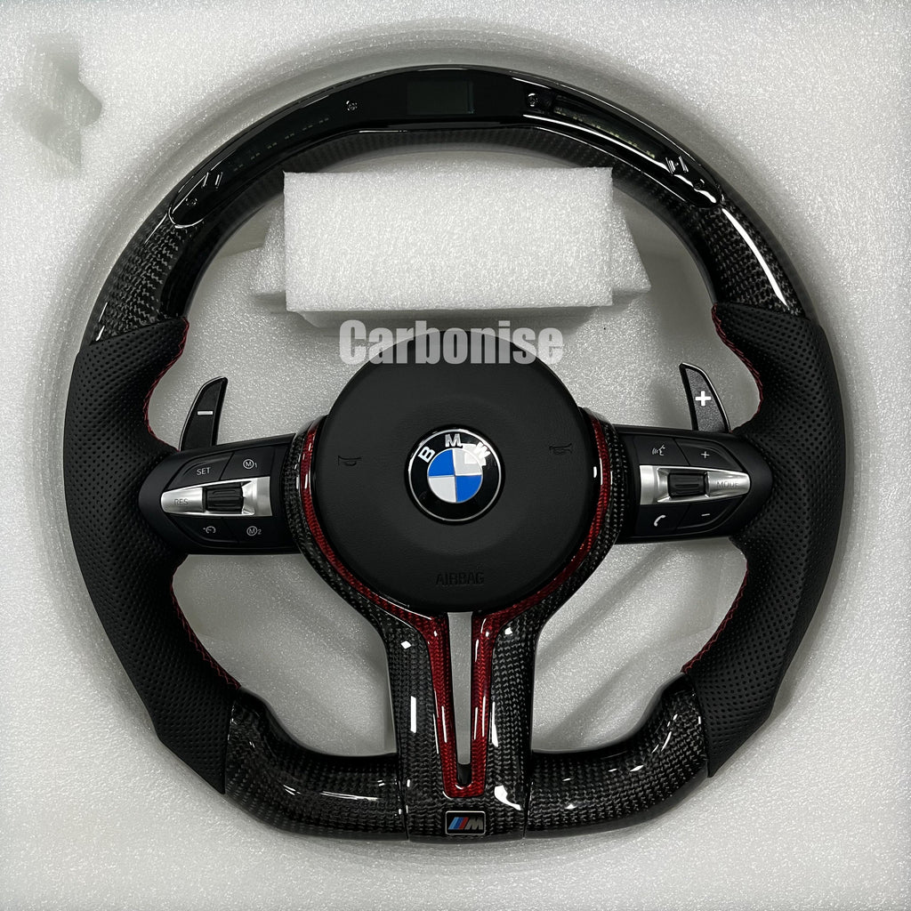 Custom BMW M steering wheel featuring gloss carbon fiber with a digital LED shift display, black perforated leather grips, and red contrast accents.