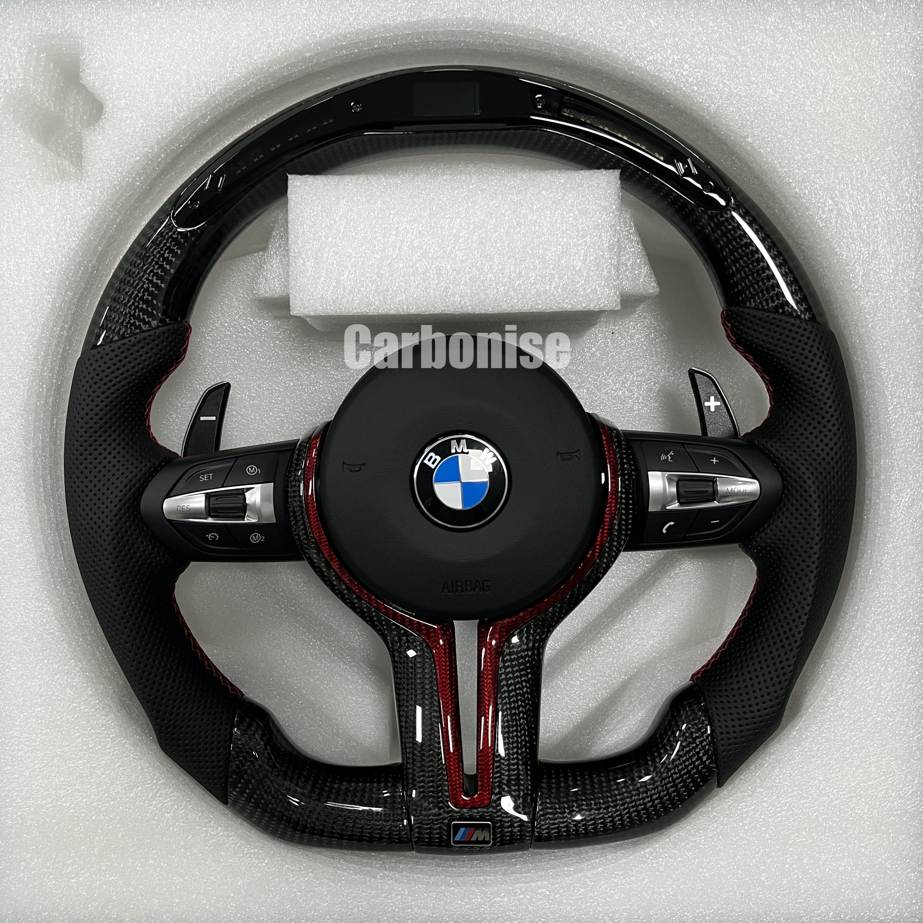 Custom BMW M steering wheel featuring gloss carbon fiber with a digital LED shift display, black perforated leather grips, and red contrast accents.