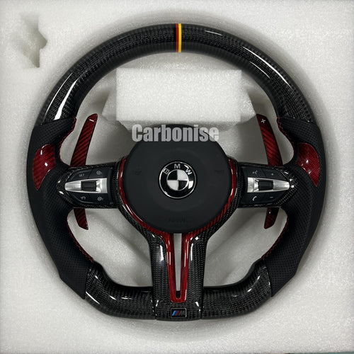 Custom BMW M steering wheel with gloss carbon fiber, a German flag racing stripe, red tinted carbon accents, and perforated leather grips with red stitching.