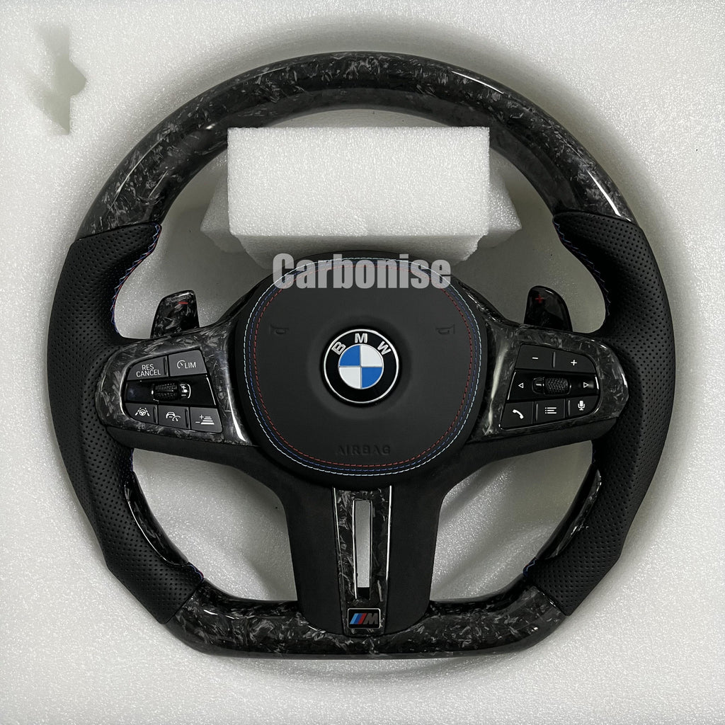 Custom BMW M performance steering wheel featuring a forged carbon fiber finish, black perforated leather side grips, and blue performance stitching.