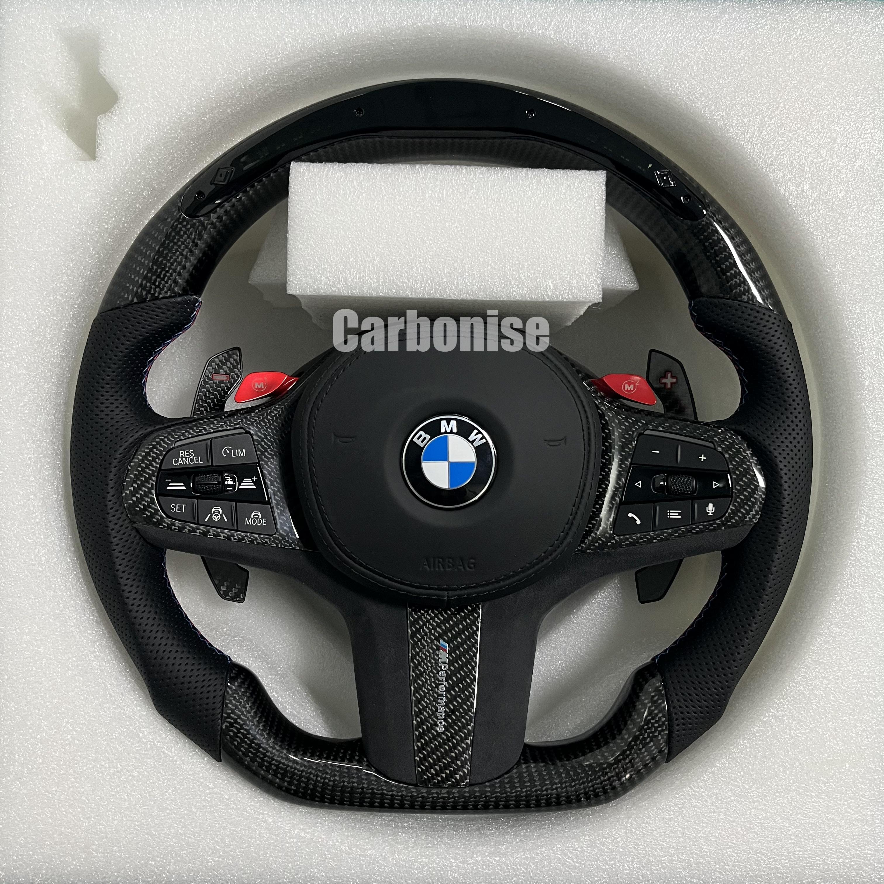 Custom BMW M performance steering wheel featuring gloss carbon fiber, black Alcantara grips, and vibrant red M1 and M2 button accents.