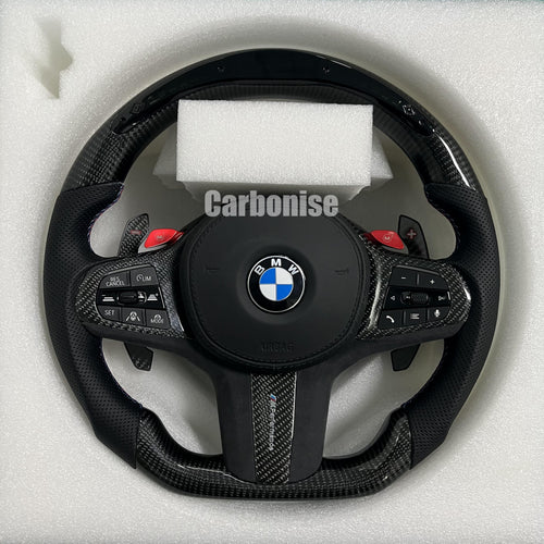 Custom BMW M performance steering wheel featuring gloss carbon fiber, black Alcantara grips, and vibrant red M1 and M2 button accents.